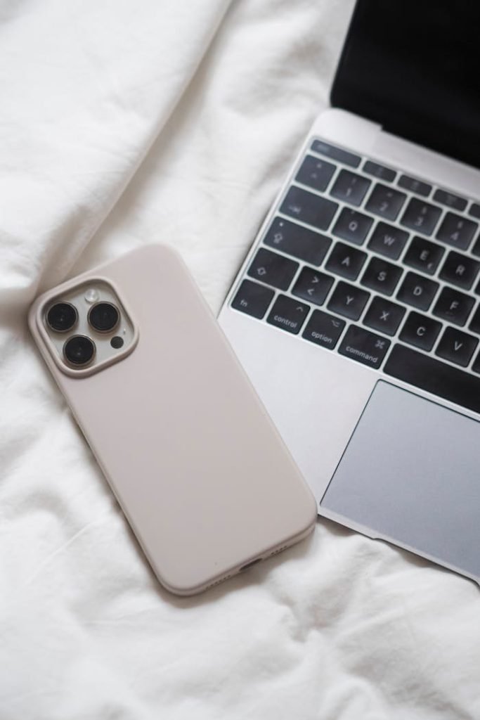 Stylish minimalism: smartphone next to laptop on a white bed, showcasing modern technology essentials.